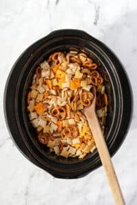A wooden spoon stirring a crock pot full of Chex Mix.