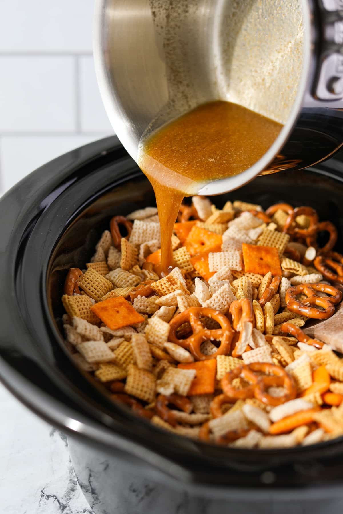 Pouring melted butter into a slow cooker filled with Chex Mix.