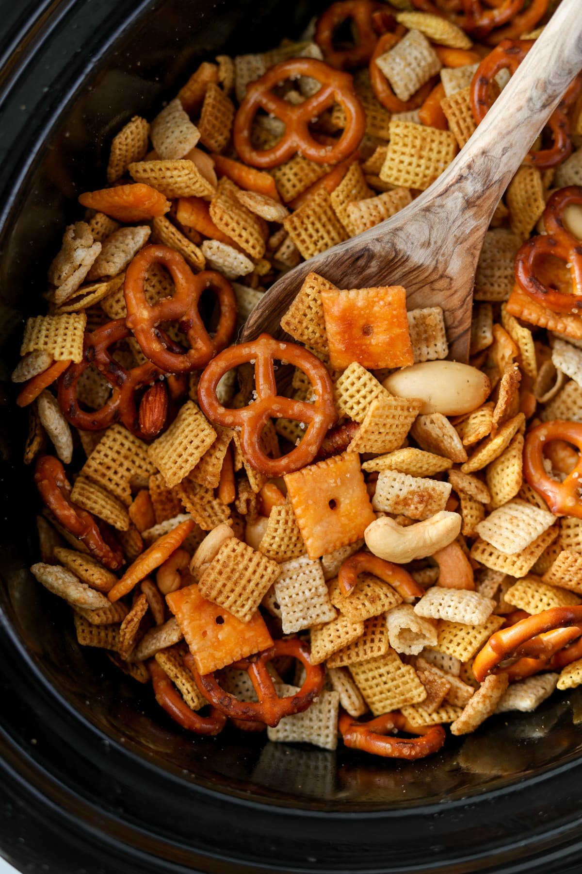Using a wooden spoon to scoop Chex Mix from a Crock Pot.