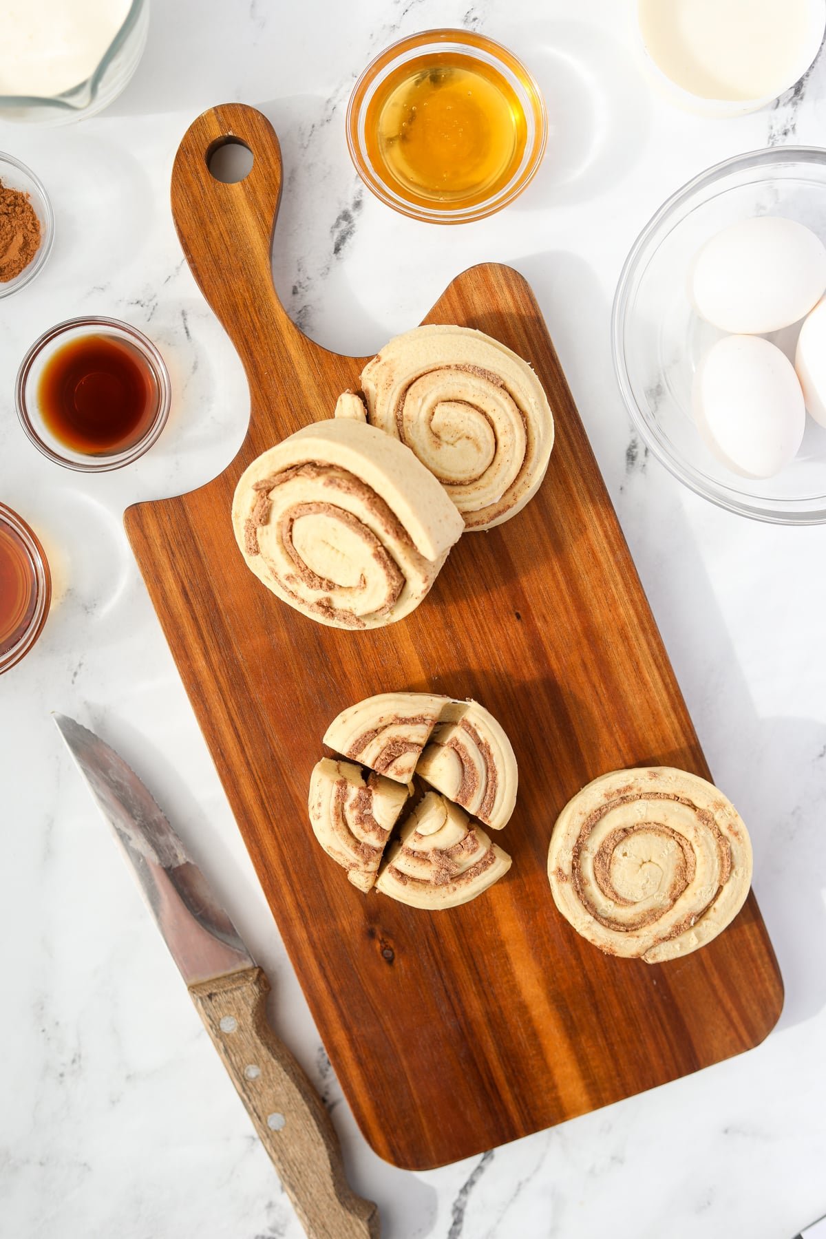 A cutting board with cinnamon rolls being sliced into quarters.