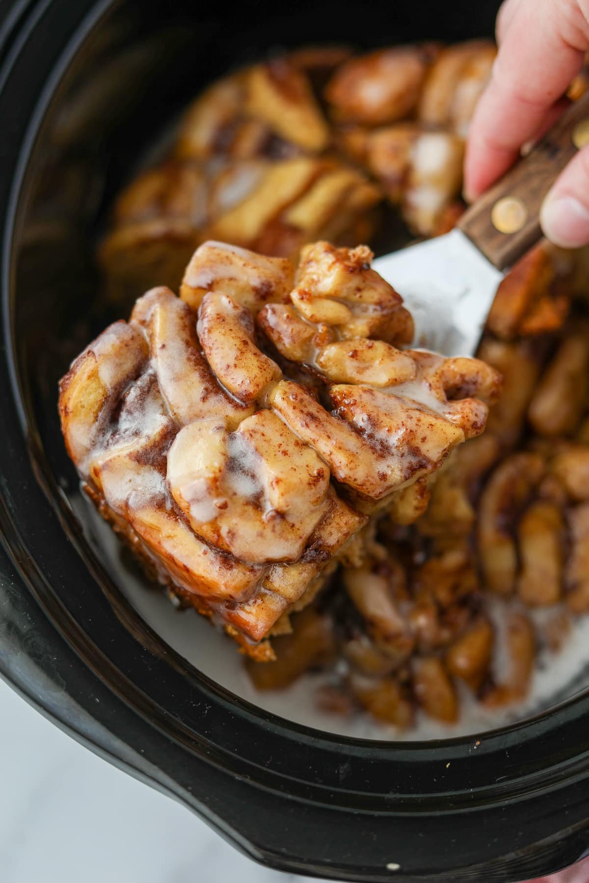 Taking a portion of crock pot cinnamon rolls from a slow cooker.