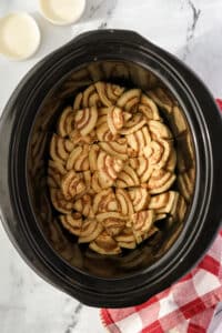 A slow cooker filled with cinnamon roll pieces.