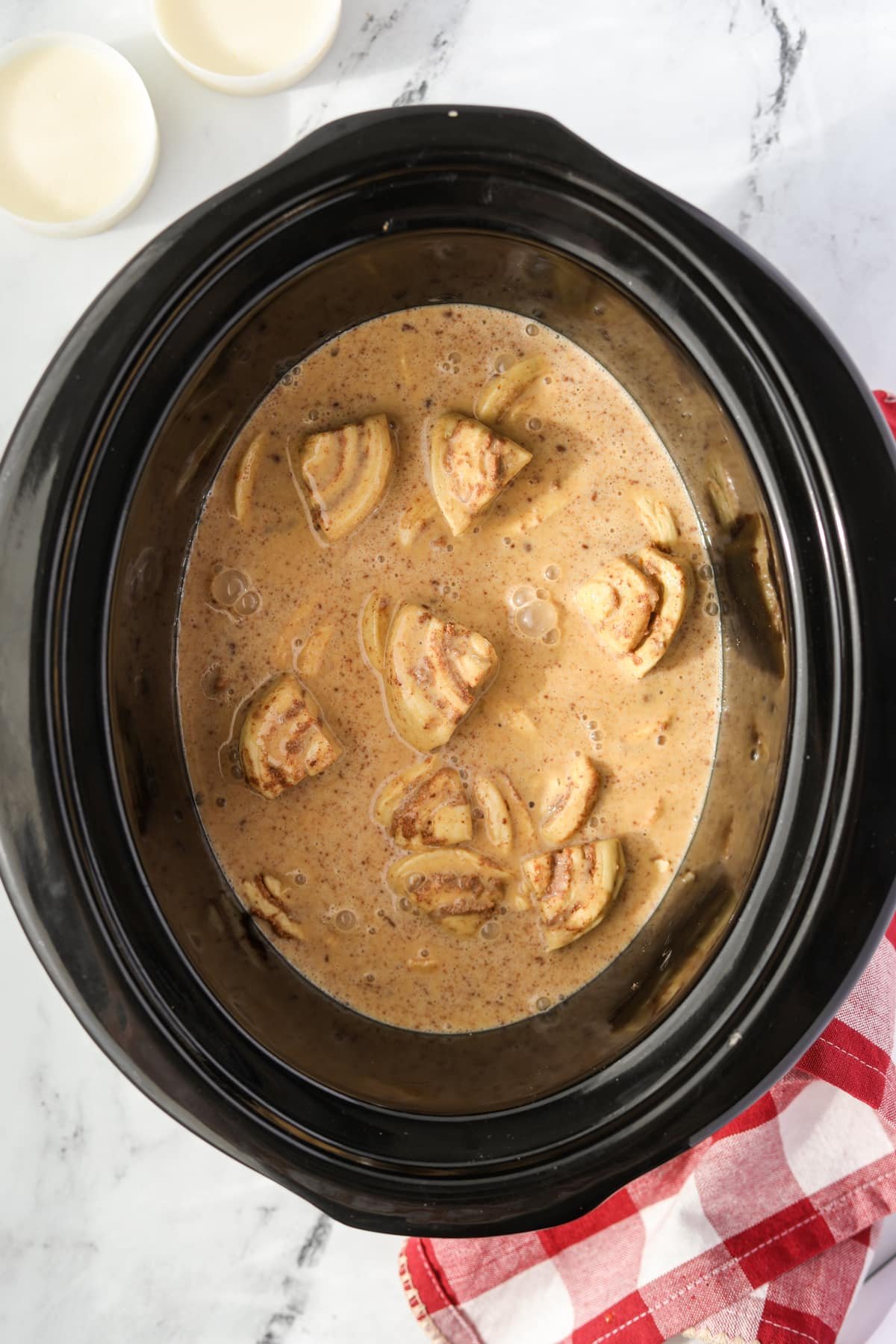 A slow cooker filled with cinnamon roll pieces and a custard mixture.