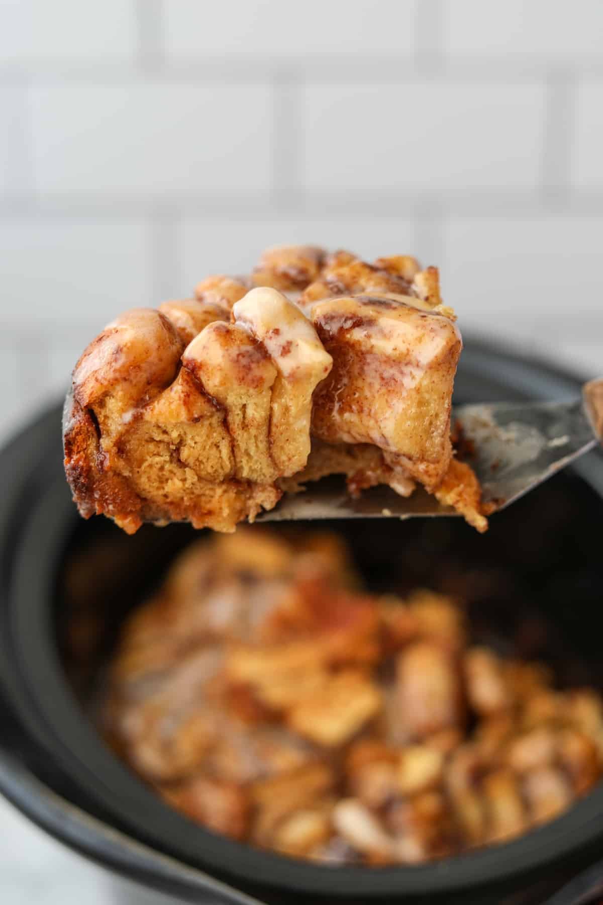 Lifting a slice of cinnamon roll casserole from a crock pot.