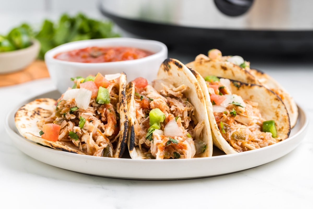 A plate of chicken tacos, with a slow cooker in the background.