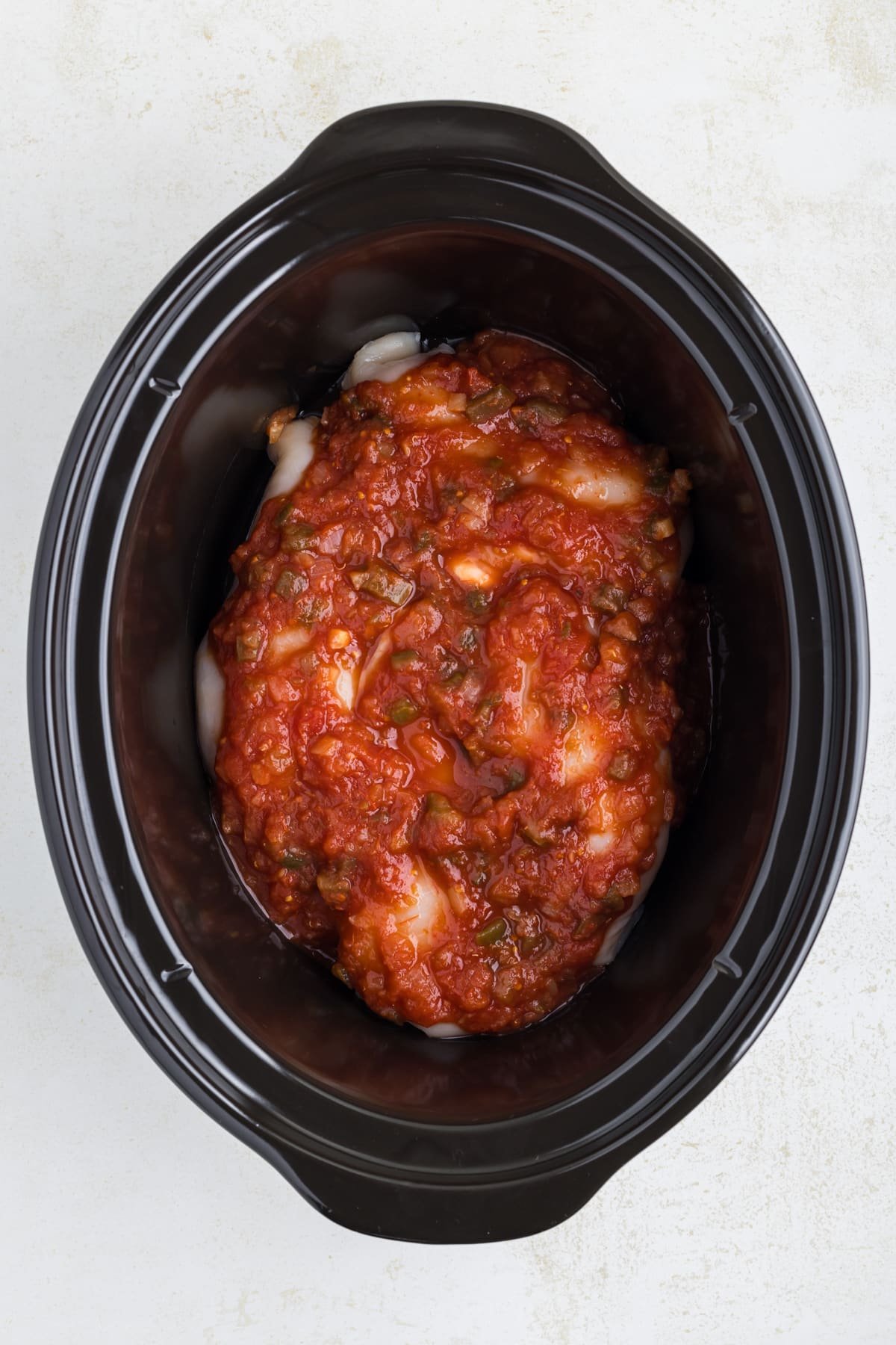 A slow cooker filled with chicken and salsa.