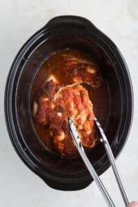 Using tongs to remove salsa chicken from a slow cooker.