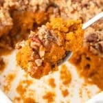 A spoon scooping a portion of sweet potato casserole from a baking dish.