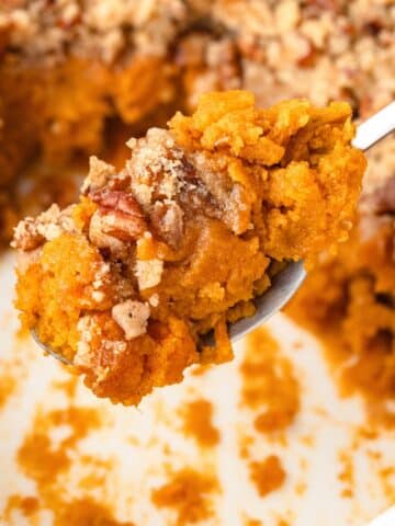 A spoon scooping a portion of sweet potato casserole from a baking dish.