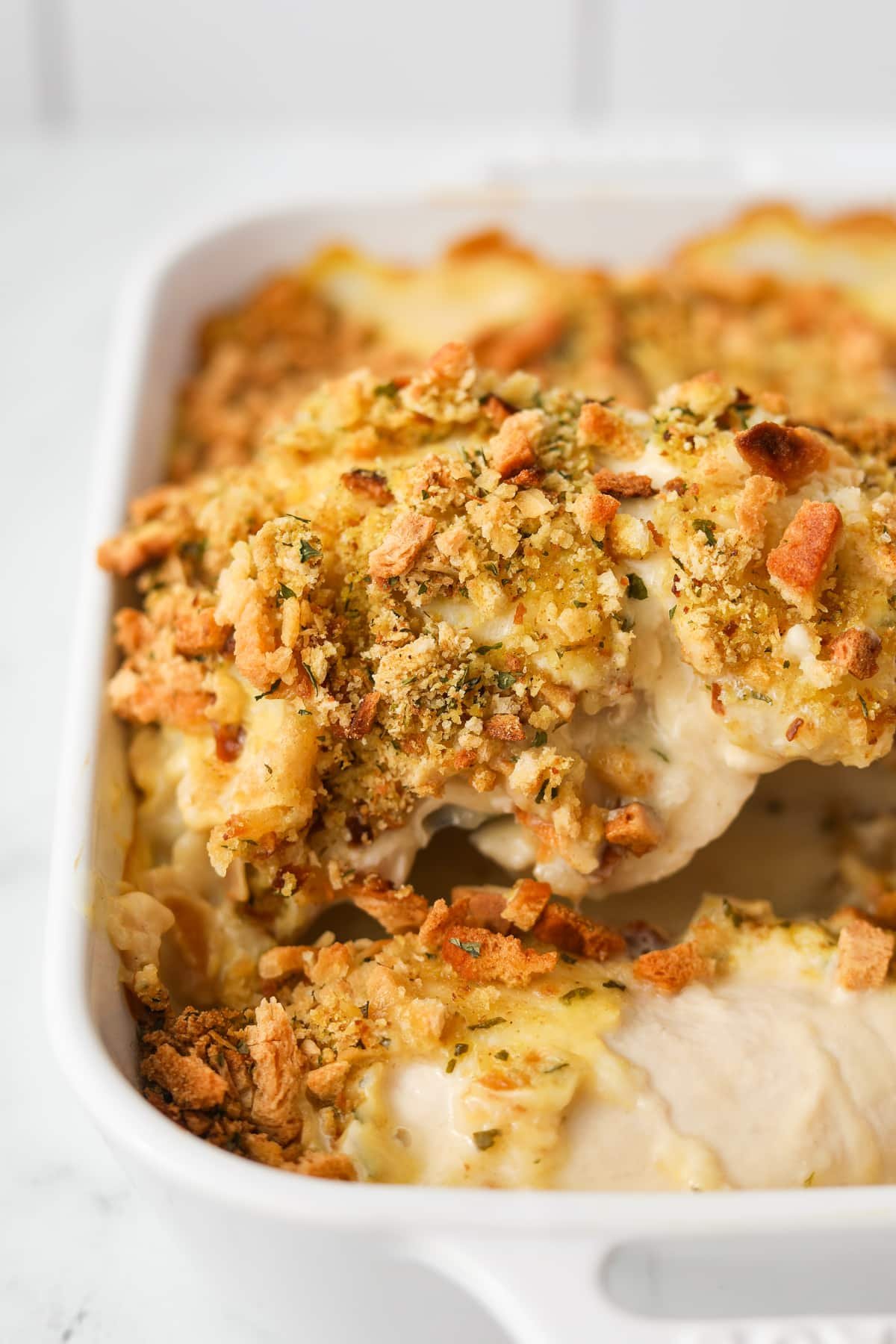 Lifting a chicken breast topped with stuffing mix from a baking dish.