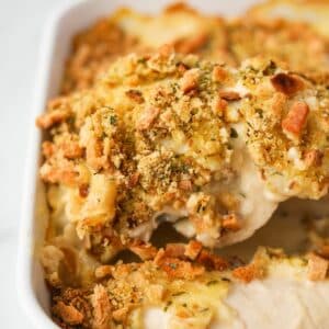 Lifting a piece of chicken and stuffing from a baking dish.