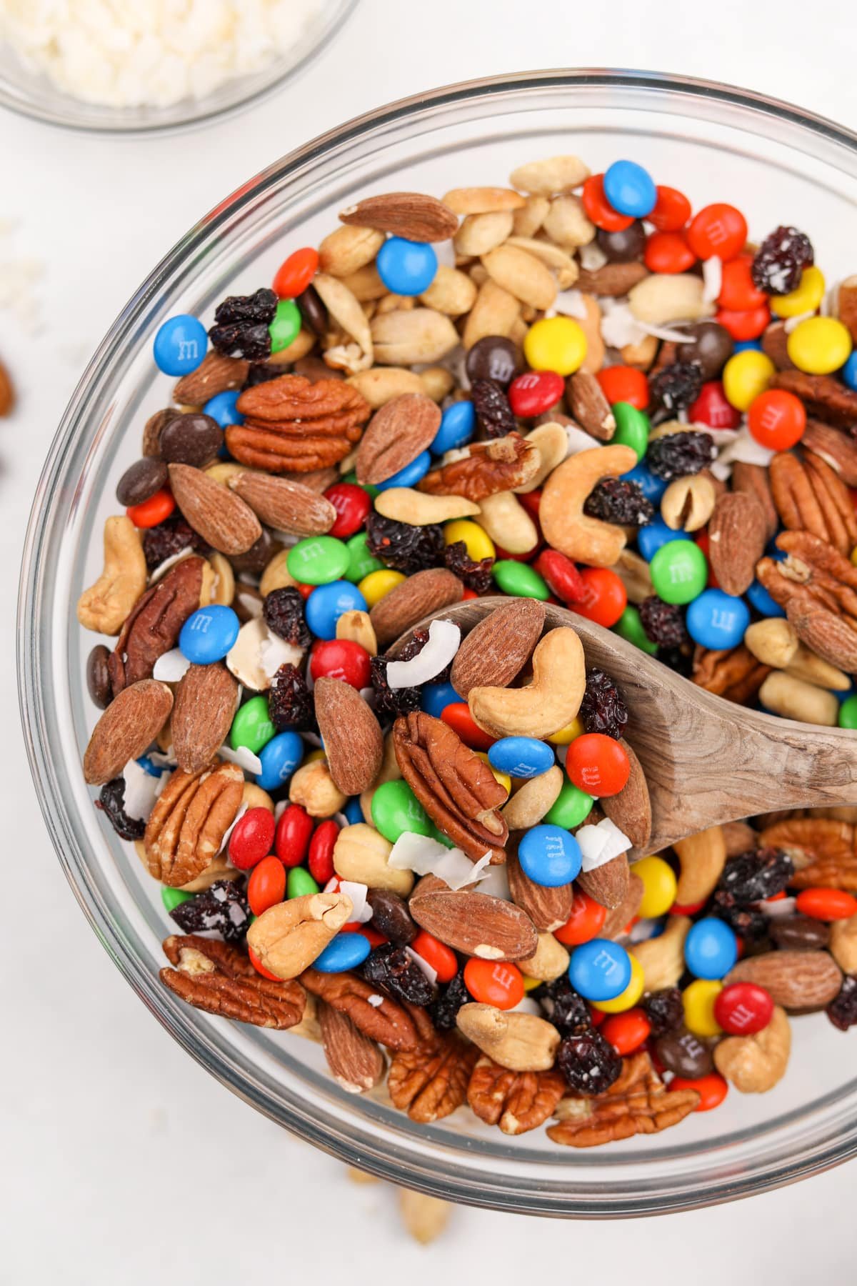 A large bowl of trail mix being scooped with a wooden spoon.