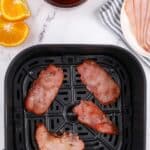An air fryer basket with four slices of cooked back bacon.