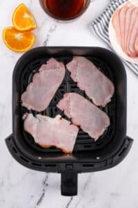An air fryer basket with canadian bacon slices inisde.