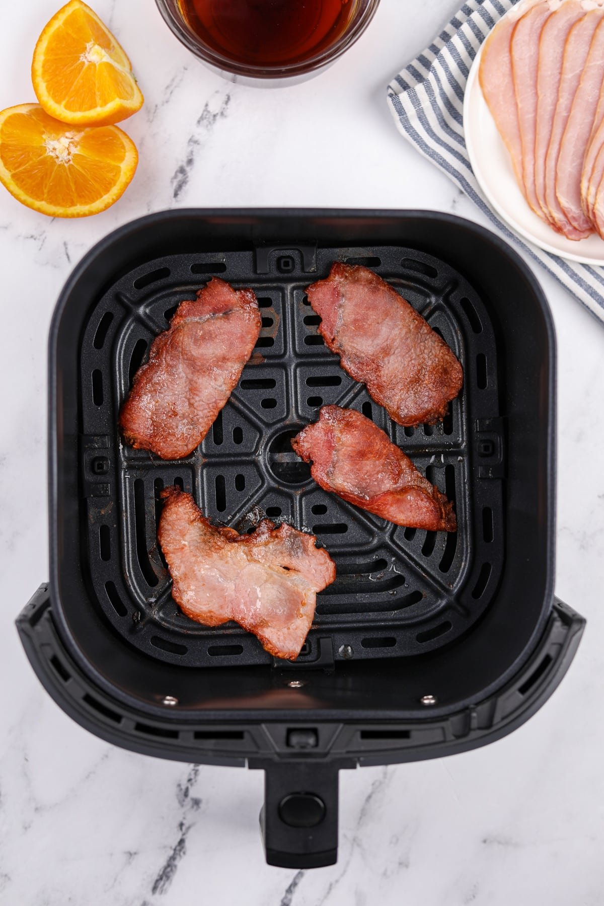 An air fryer basket with four slices of cooked back bacon inside.