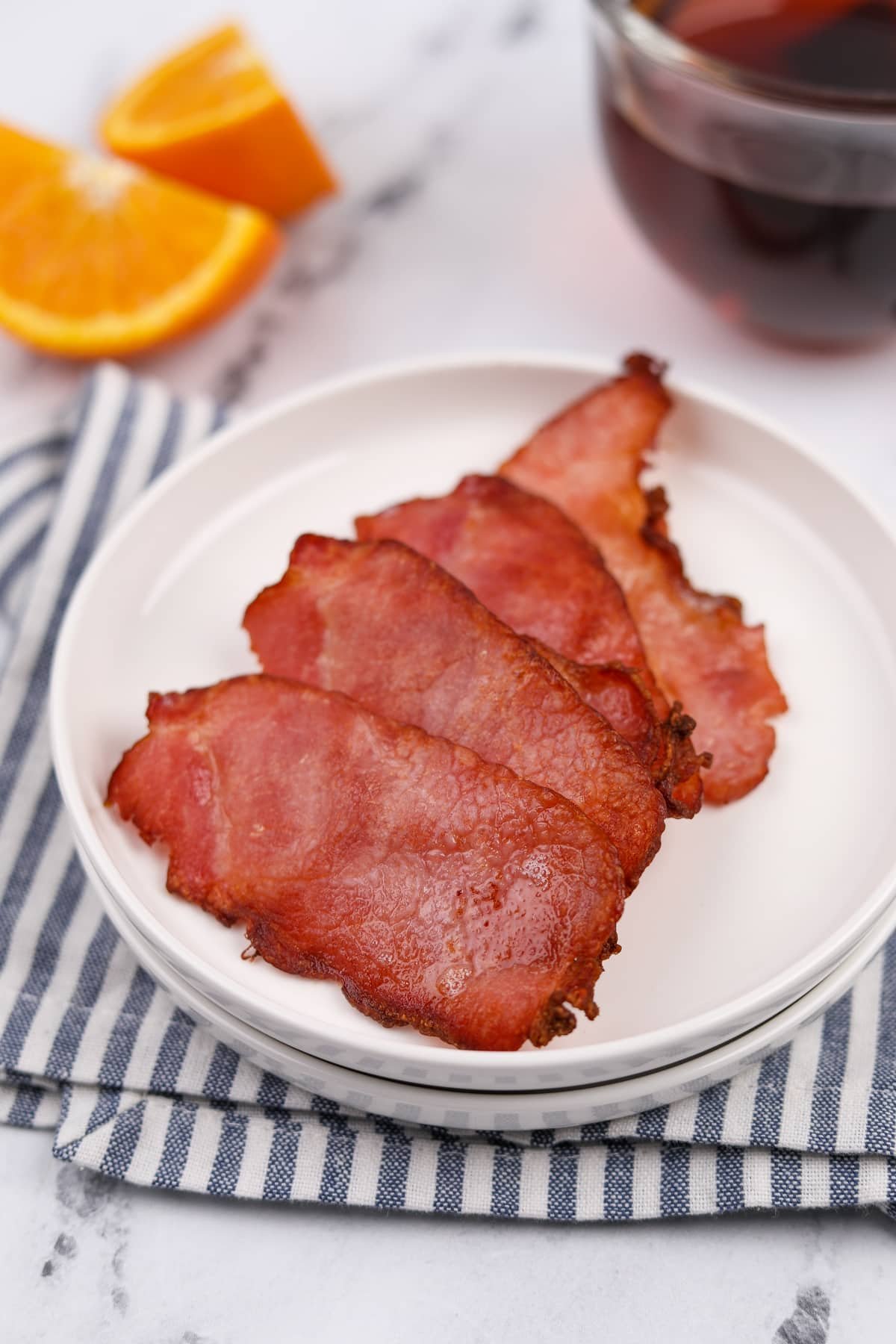 A plate resting on a striped napkin with four slices of Canadian bacon.