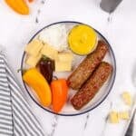 A plate filled with veggies, chicken sausages, cottage cheese, and mustard.