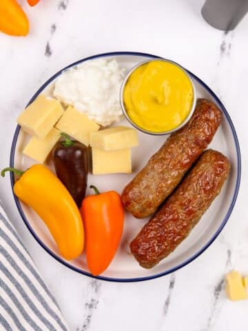 A plate filled with veggies, chicken sausages, cottage cheese, and mustard.