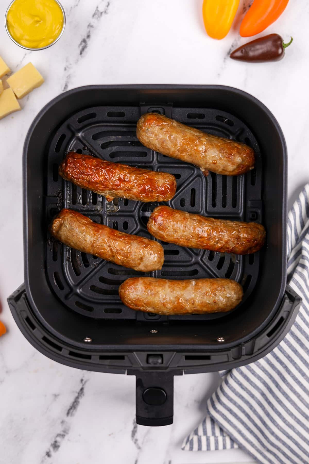 An air fryer basket with cooked sausages inside.