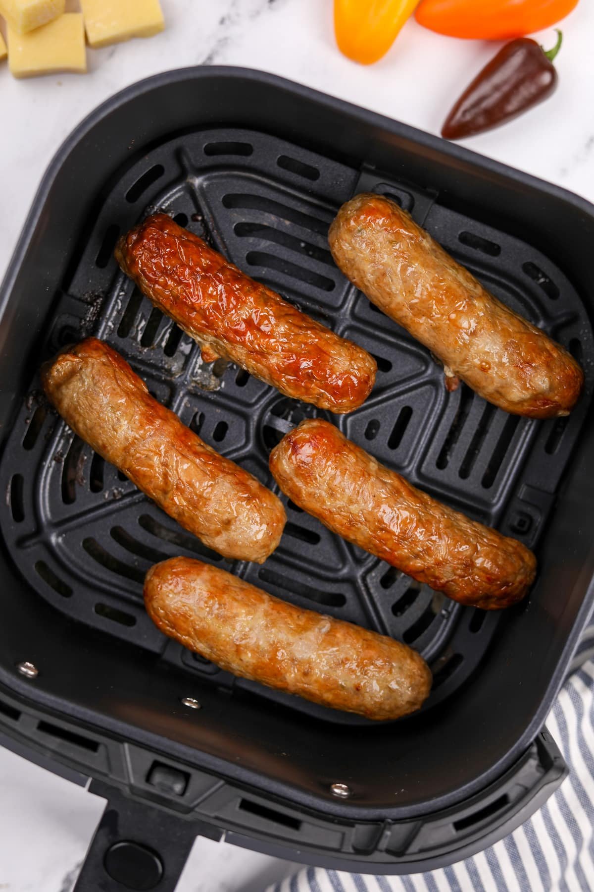 An air fryer basket with cooked sausages inside.