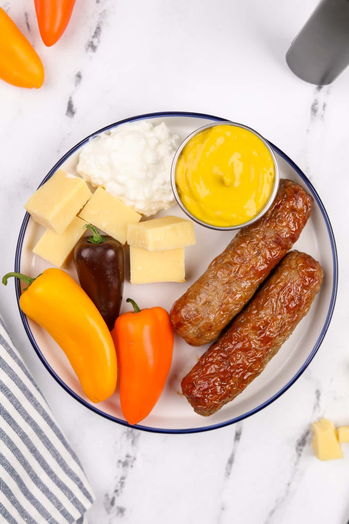 A plate filled with veggies, sausages, mustard, and cottage cheese.