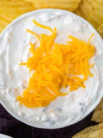 A bowl of creamy dip topped with cheese, with chips around the side.