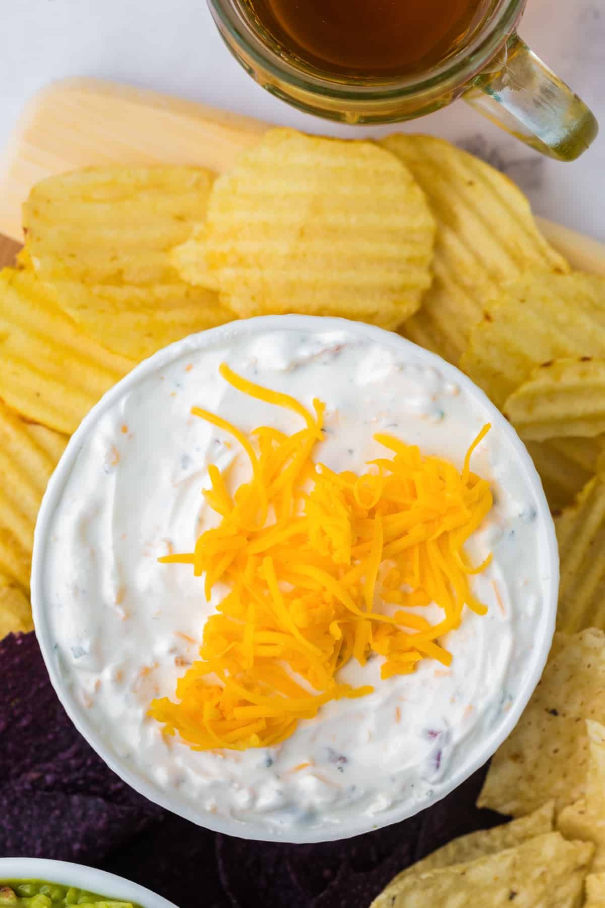 A bowl of cream cheese dip topped with cheddar cheese, with ruffled potato chips on the side.