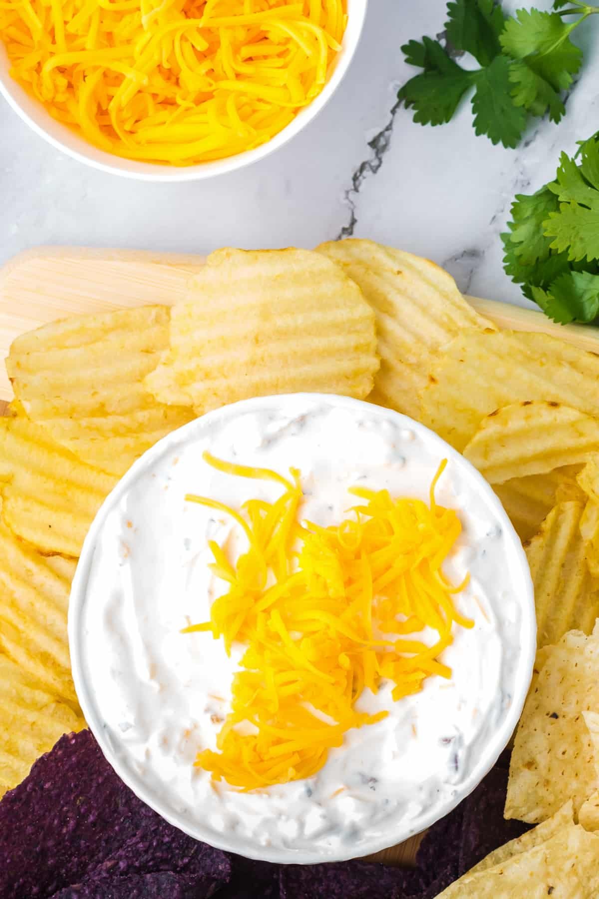 A small bowl of creamy dip topped with shredded cheddar cheese, with ridged potato chips on the side.