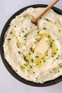A black bowl filled with mashed potatoes and topped with melted butter and chives.