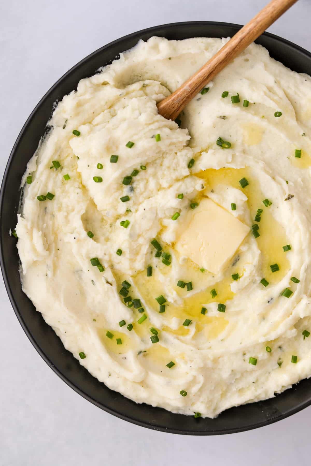 A black bowl filled with mashed potatoes and topped with melted butter and chives.