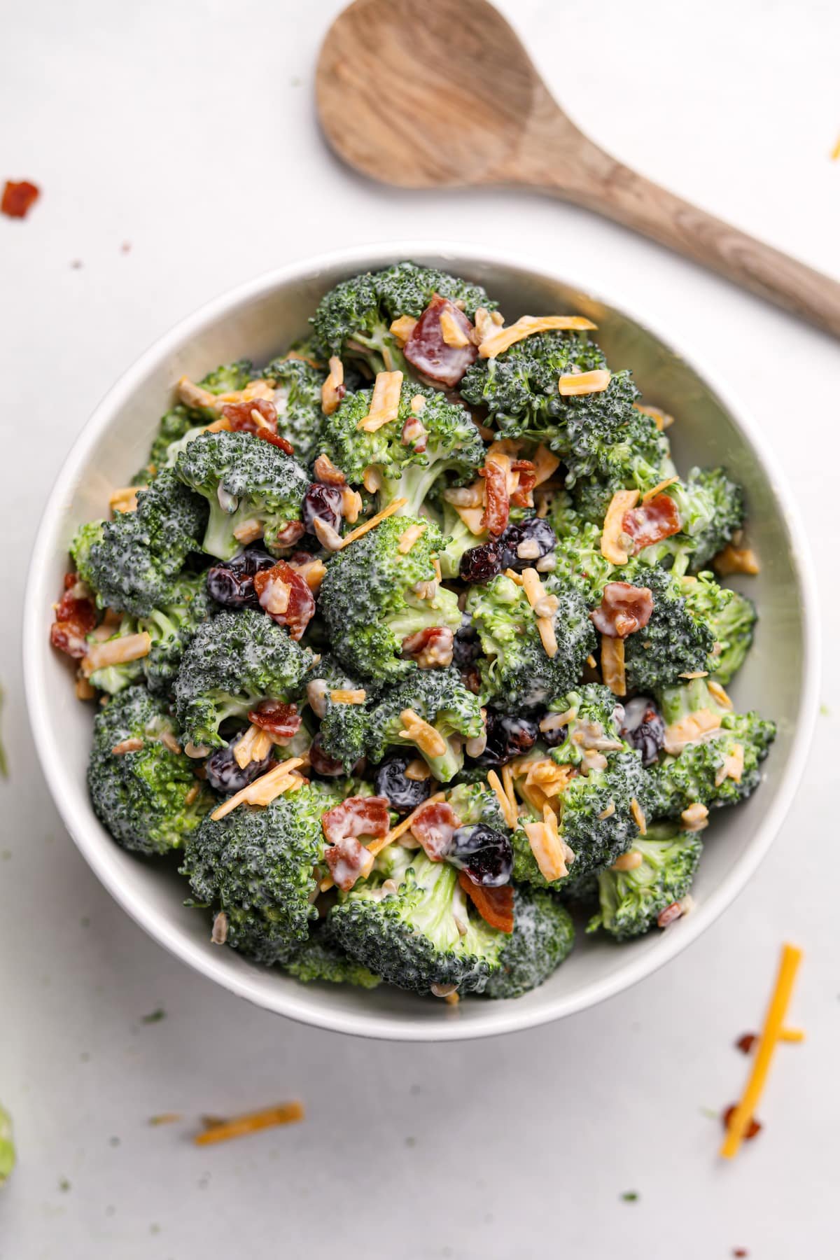 A white bowl filled with broccoli salad that's been garnished with bacon and cheddar cheese.