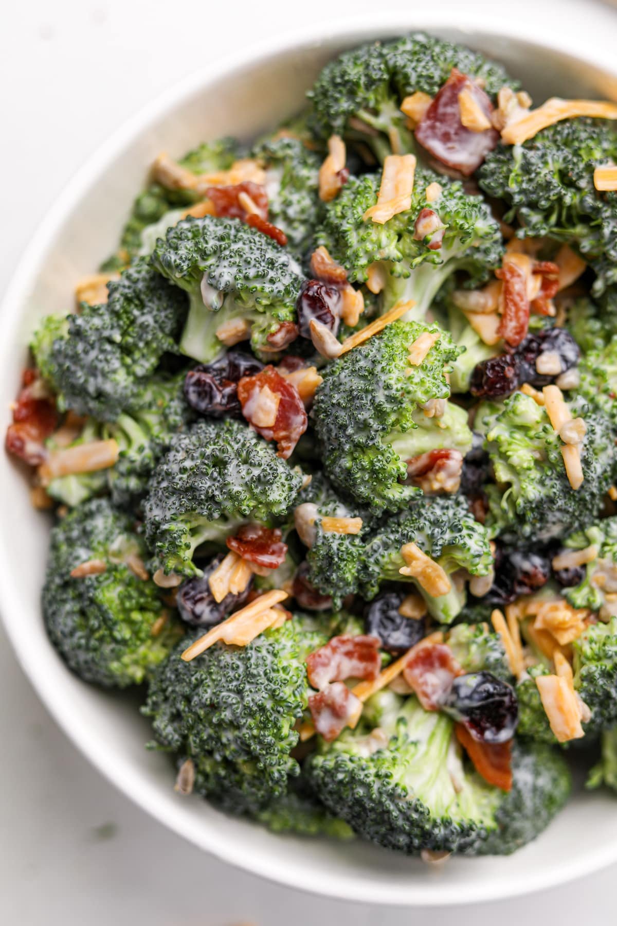 A close up of a bowl of broccoli salad featuring bacon crumbles and cheddar cheese shreds.