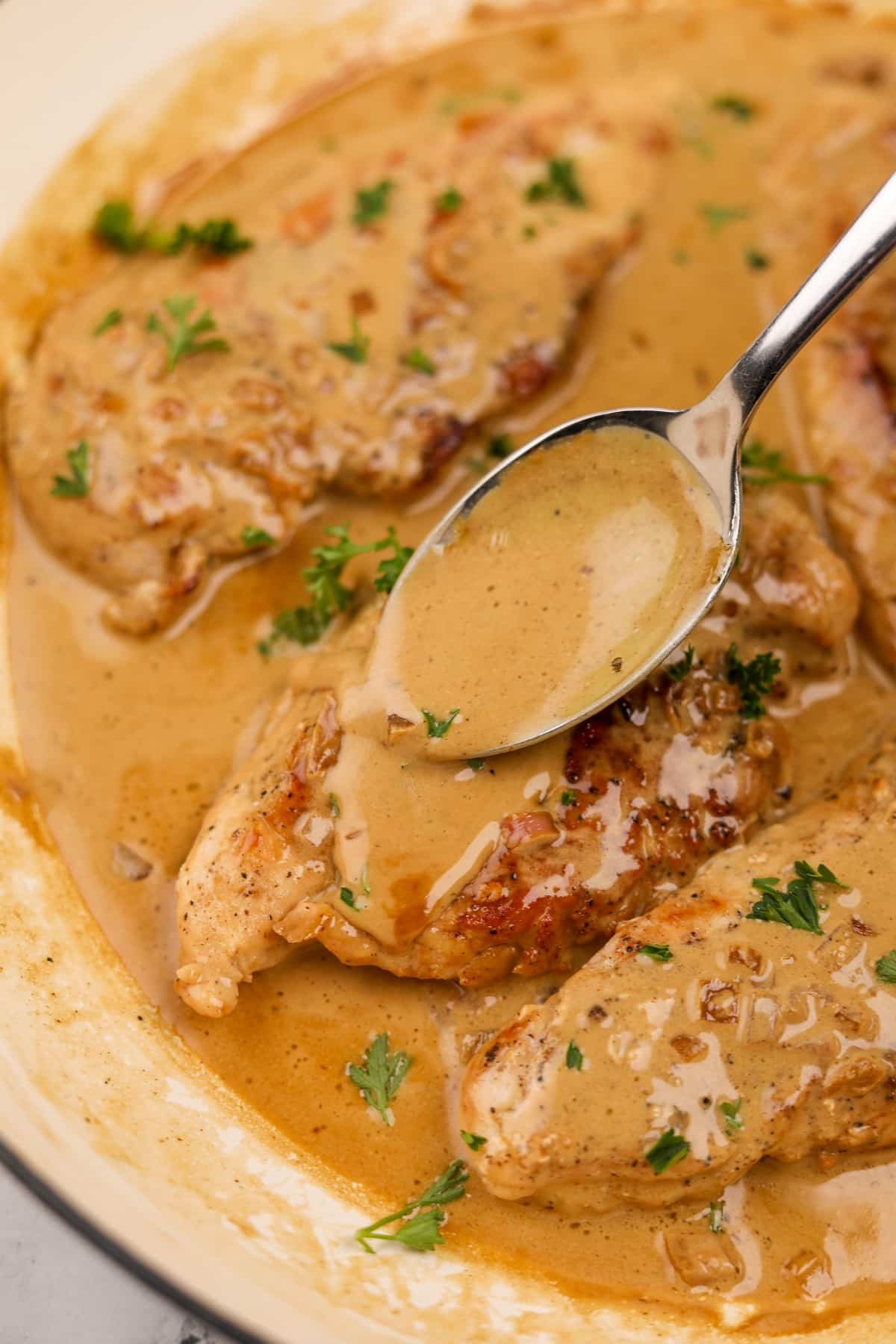 Spooning sauce on top of cooked chicken breasts.