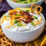 A bowl of loaded baked potato dip topped with shredded cheese, bacon, and green onion.