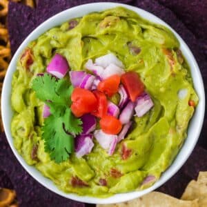 A bowl of guacamole topped with red onion, tomato, and cilantro.