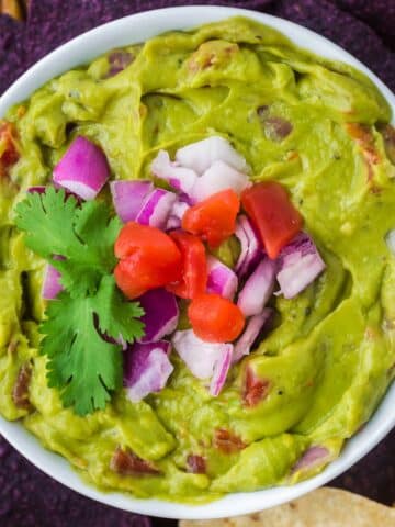 A bowl of guacamole topped with red onion, tomato, and cilantro.