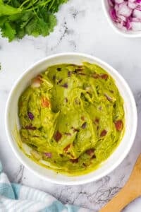 A bowl of guacamole featuring chunks of tomato.