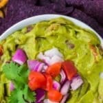 A bowl of guacamole topped with red onion and tomato.