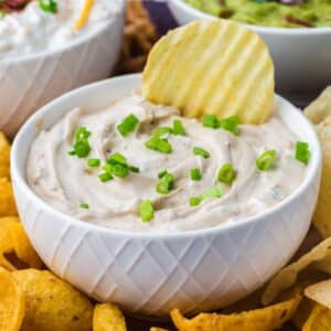 A small bowl of onion dip garnished with green onions, with a ridged potato chip wedged into the dip.