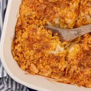 A wooden spoon scooping from a baking dish of hash brown casserole.