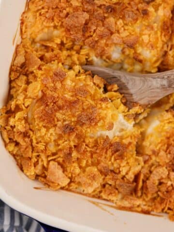 A wooden spoon scooping from a baking dish of hash brown casserole.