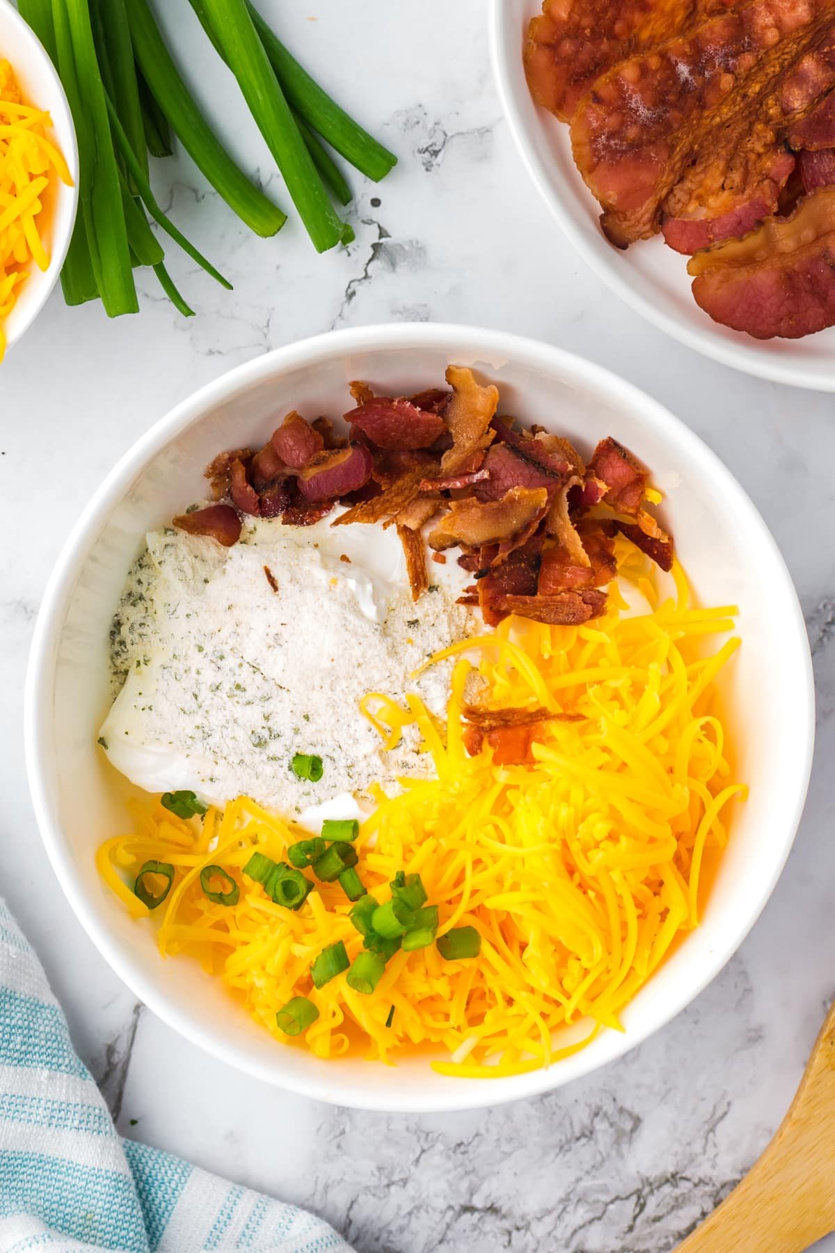 A white bowl featuring shredded cheese, bacon, ranch, and green onions.