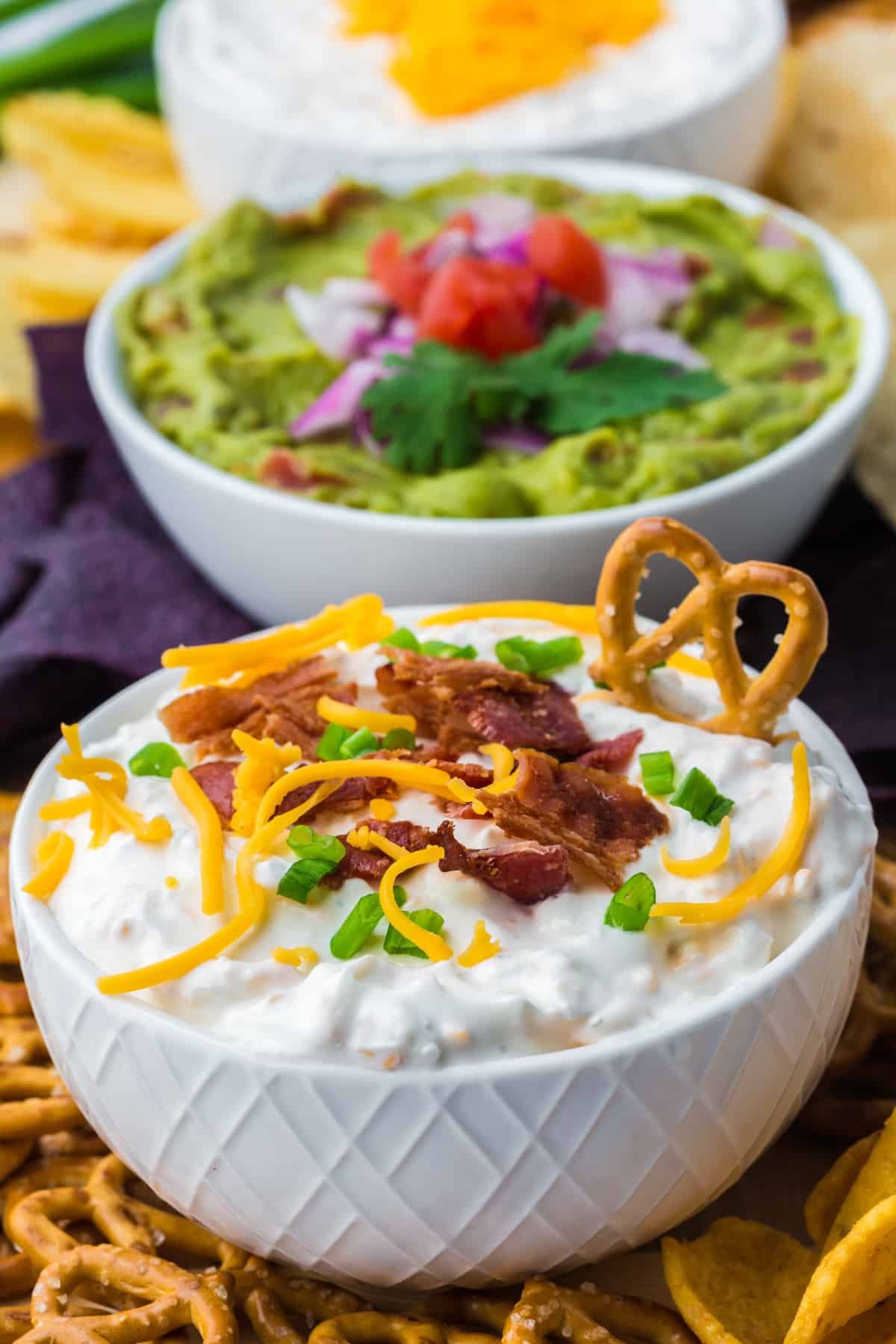 A bowl of baked potato dip with a pretzel dipped on the side.