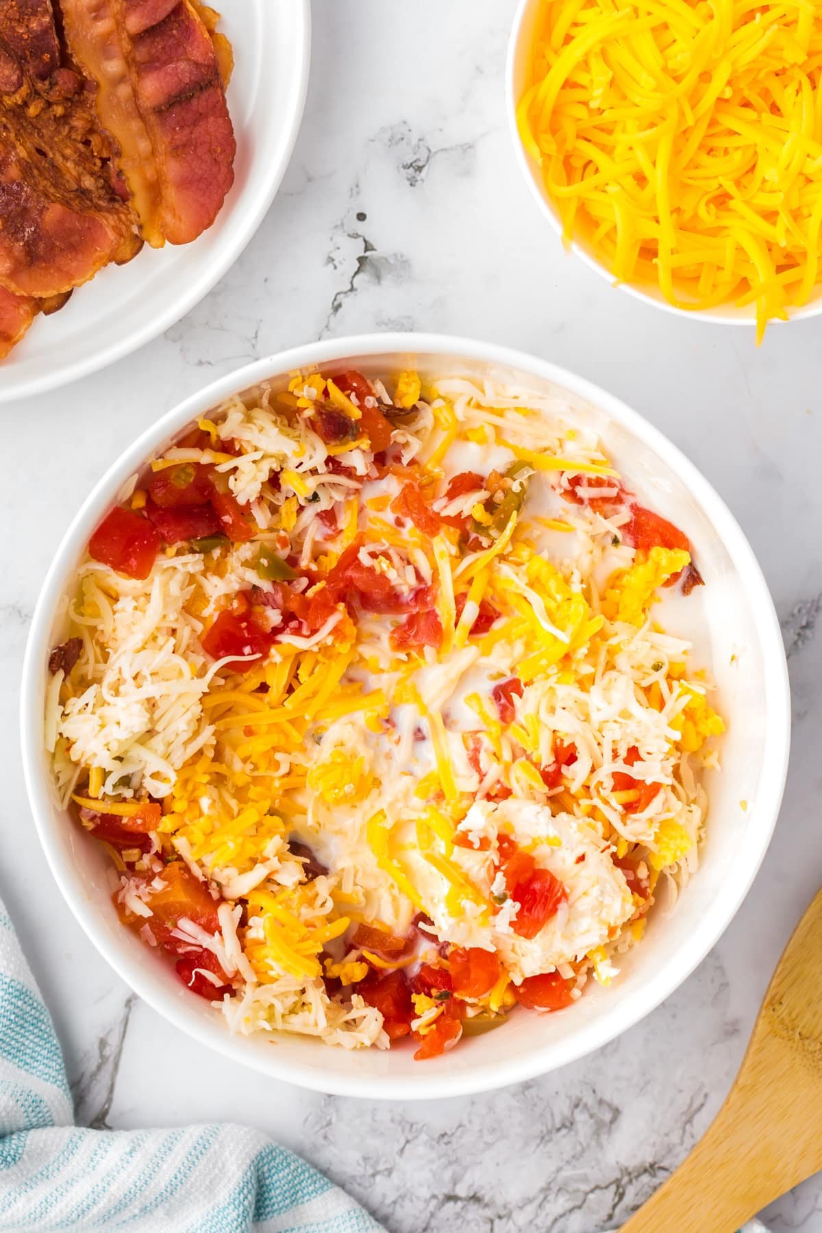 A large bowl with cheese and cream cheese being mixed together with bacon and rotel tomatoes.
