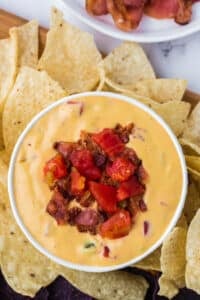 A small bowl of nacho cheese dip garnished with bacon and tomato.