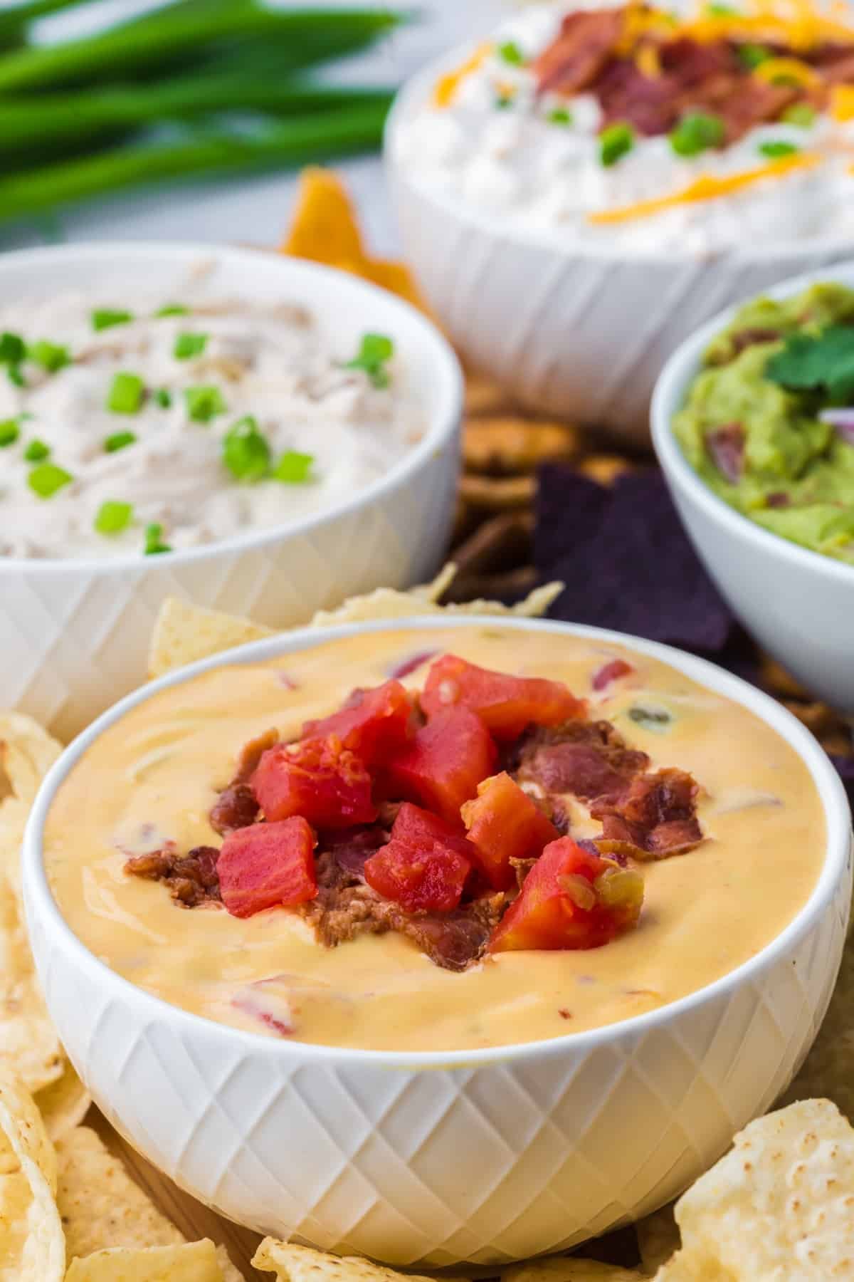 A bowl of nacho cheese dip garnished with bacon and tomatoes.