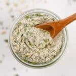 An overhead view of a jar of homemade ranch seasoning, with a small wooden spoon scooping some out.