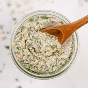 An overhead view of a jar of homemade ranch seasoning, with a small wooden spoon scooping some out.