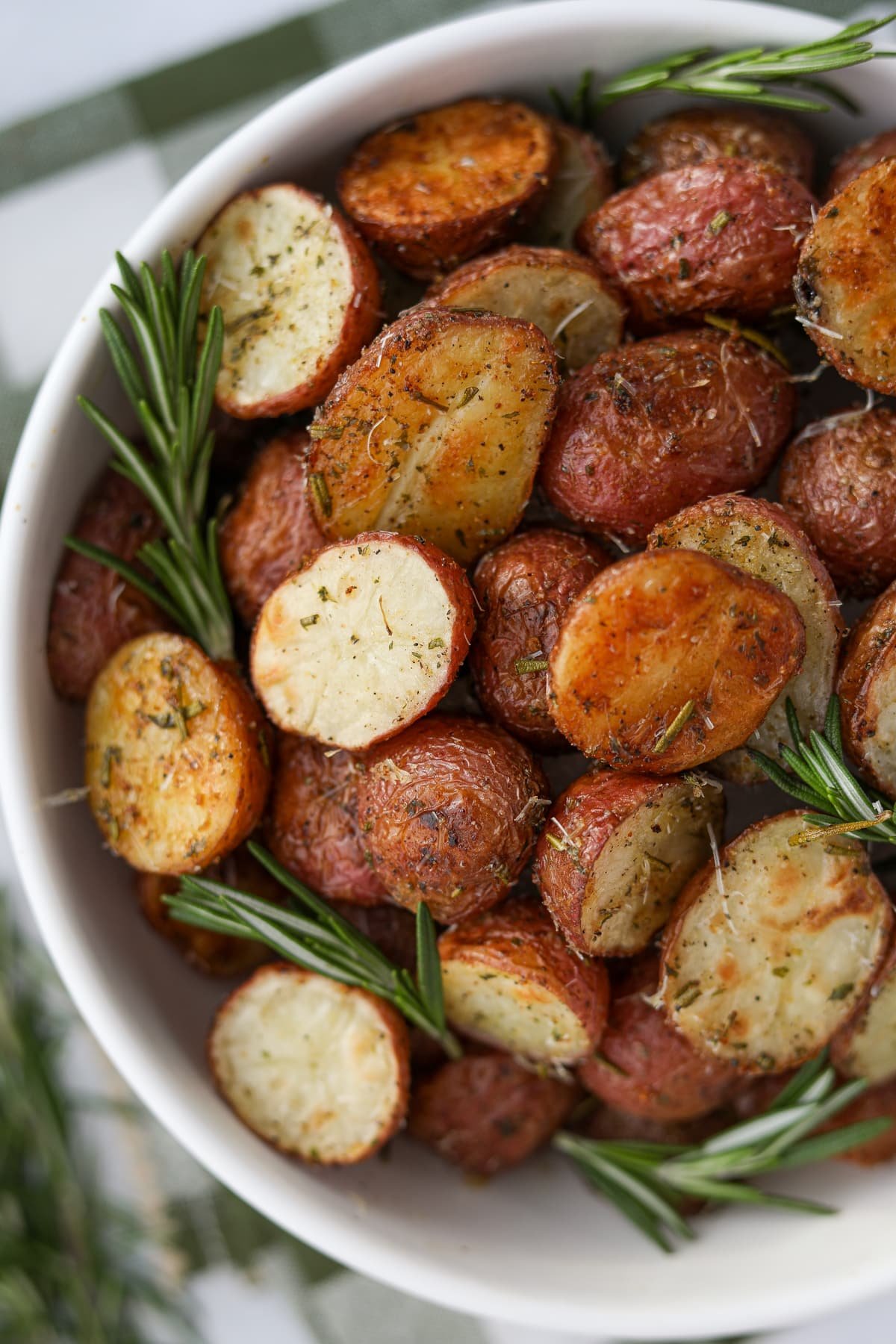 A bowl of halved, roasted baby potatoes garnished with several sprigs of fresh rosemary.