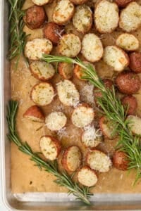 A sheet pan of roasted baby potatoes, garnished with parmesan cheese and rosemary sprigs.